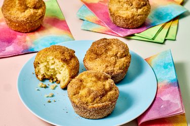Three cinnamon sugar coated muffins on a blue plate with colorful napkins nearby