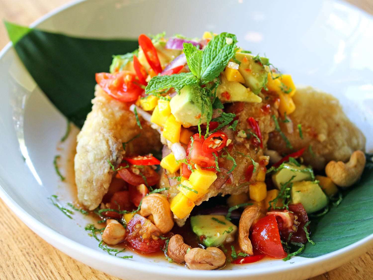 A plate of paa tod: crispy fried catfish fillets topped with diced mango, cashews, tomato, herbs, and diced avocado.