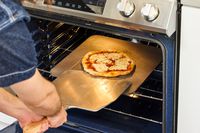 A person transferring a baked pizza from the pizza steel onto a pizza peel.