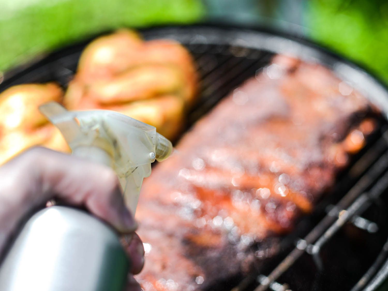 Hand holding spray bottle to mist barbecued ribs on the grill 