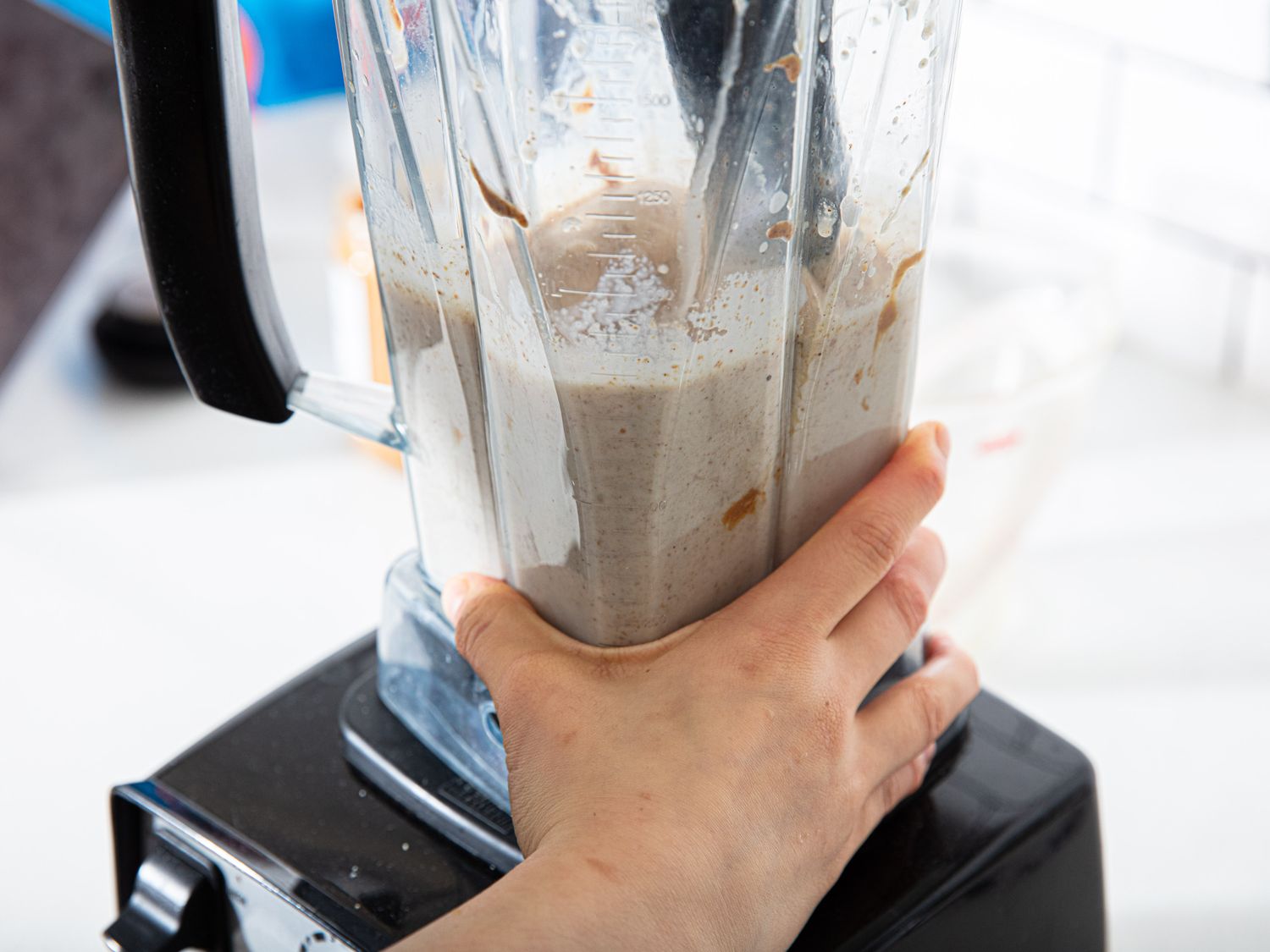 A hand holding a blender filled with a mixture over a counter