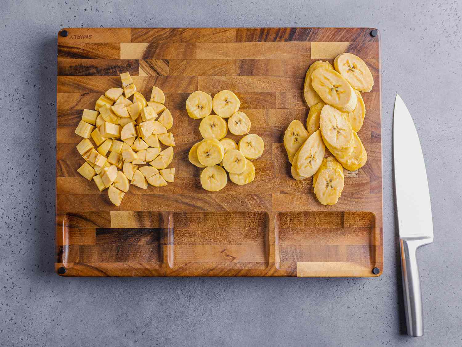 Overhead view of plantains cut in ½-inch dice, 1/3 inch thick rounds, or 1/3 inch thick slices on a wooden cutting board