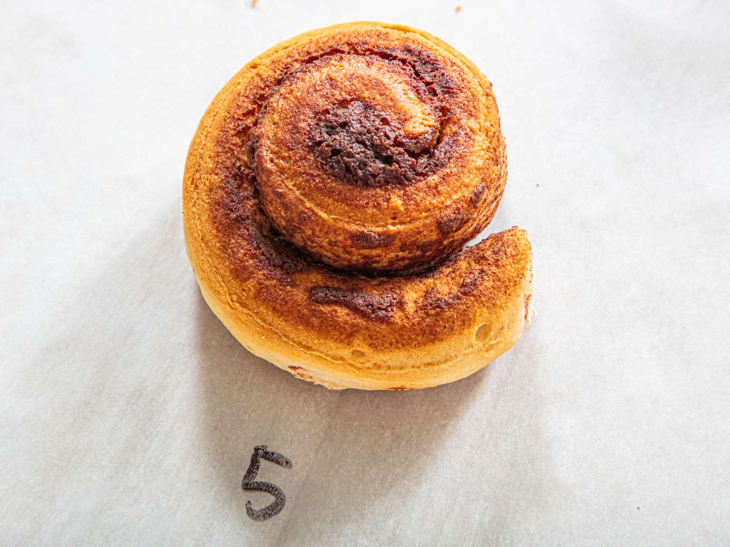 A cinnamon roll on parchment paper with the number 5 written below it