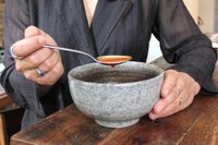 A person scooping soup out of a bowl with a spoon from the Lenox Portola 65-Piece Flatware Set
