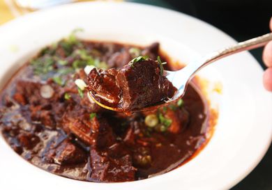 A spoonful of Texas chili con carne is held up to the camera. A bowl of chili is visible in the background.