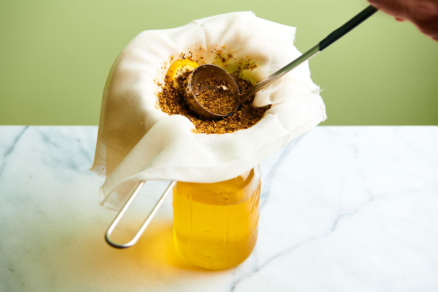 Straining cordial through cheesecloth into glass quart-size mason jar, pressing down to extract liquid.