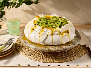 A pavlova dessert topped with kiwi and passionfruit slices on a table
