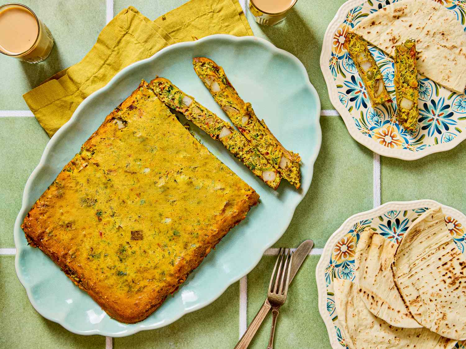 A baked dish with slices on a plate accompanied by flatbreads on another plate and a fork