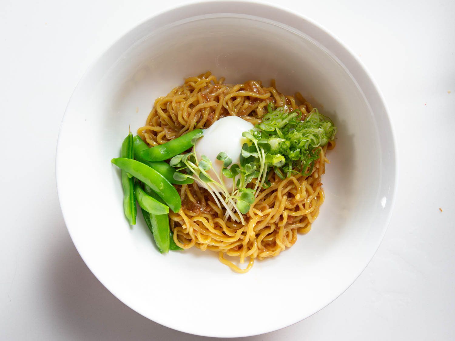 Overhead view of XO mazemen with sugar snap peas, onsen egg, and scallions in a white bowl.