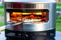 Pizza being cooked in an outdoor stainless steel Solo Stove Pi Prime, a peel positioned for retrieval