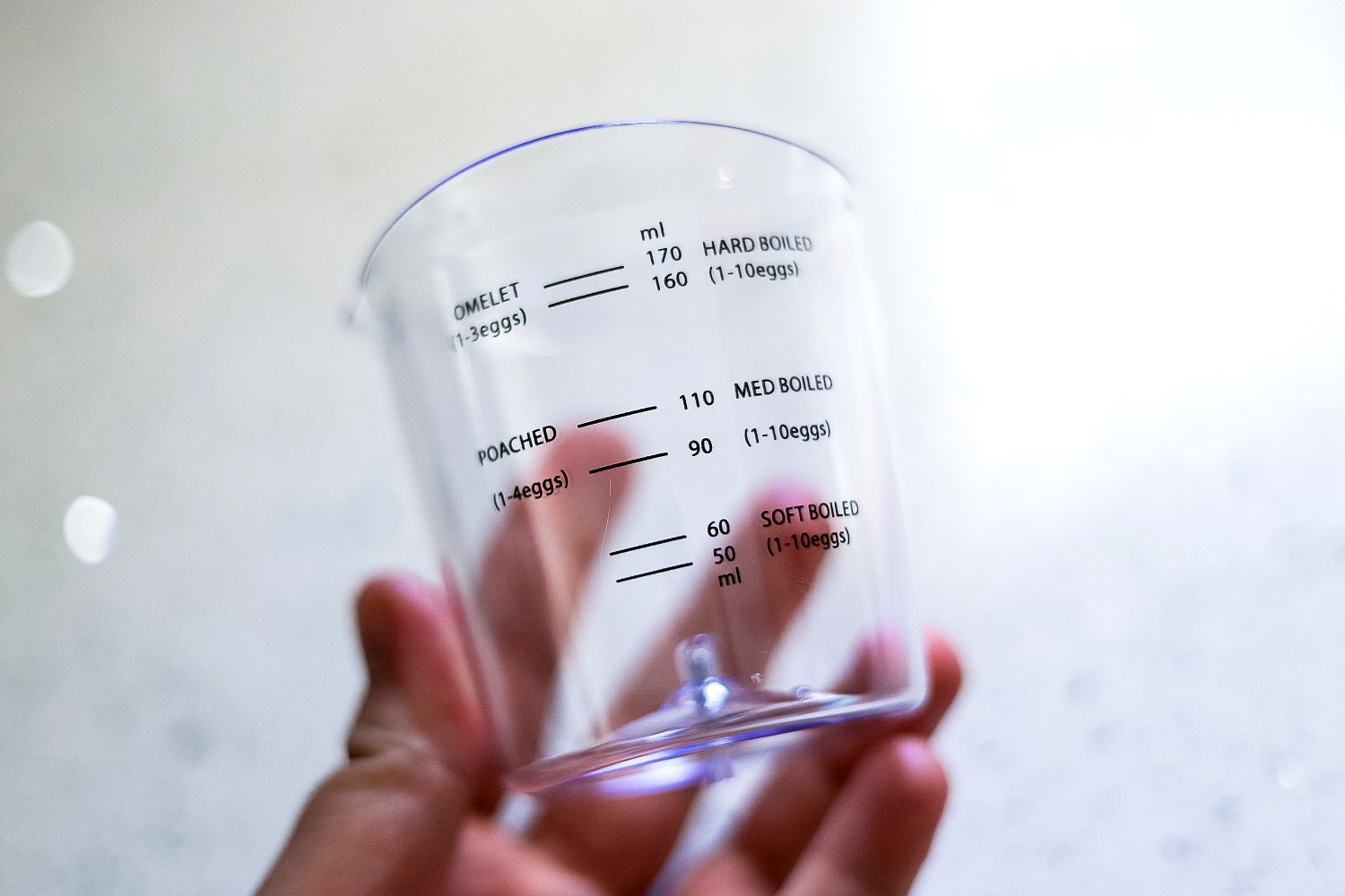 A hand holding the measuring cup from an egg cooker