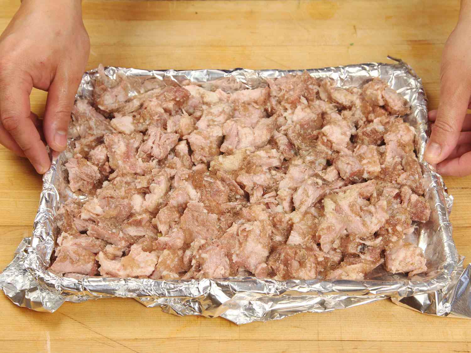 Placing shredded sous vide carnitas on a foil-lined baking sheet before crisping in the broiler.