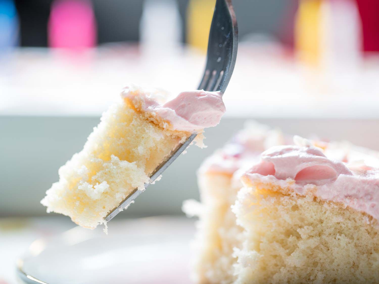 A piece of yellow cake with pink vanilla buttercream frosting on a fork. 