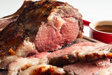 Sliced prime rib roast on a wooden board red dish in the background
