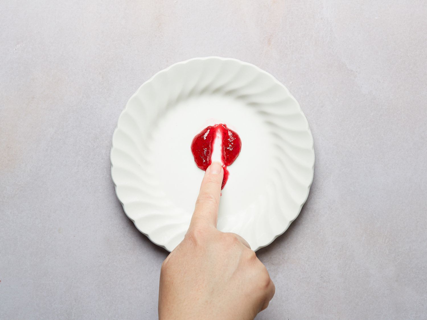 a small white plate, with a finger running a across a small sample of cranberry sauce