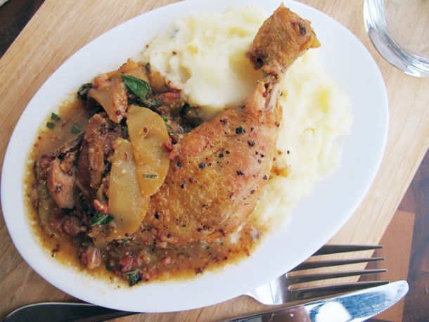 Cider-braised chicken with apples, bacon, and sage plated with mashed potatoes.