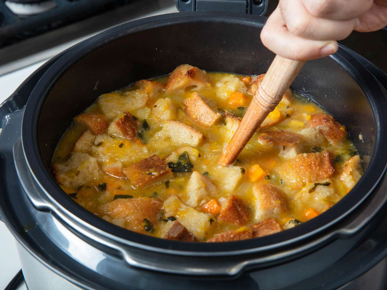 Stirring bread into a pot of ribollita made in a pressure cooker