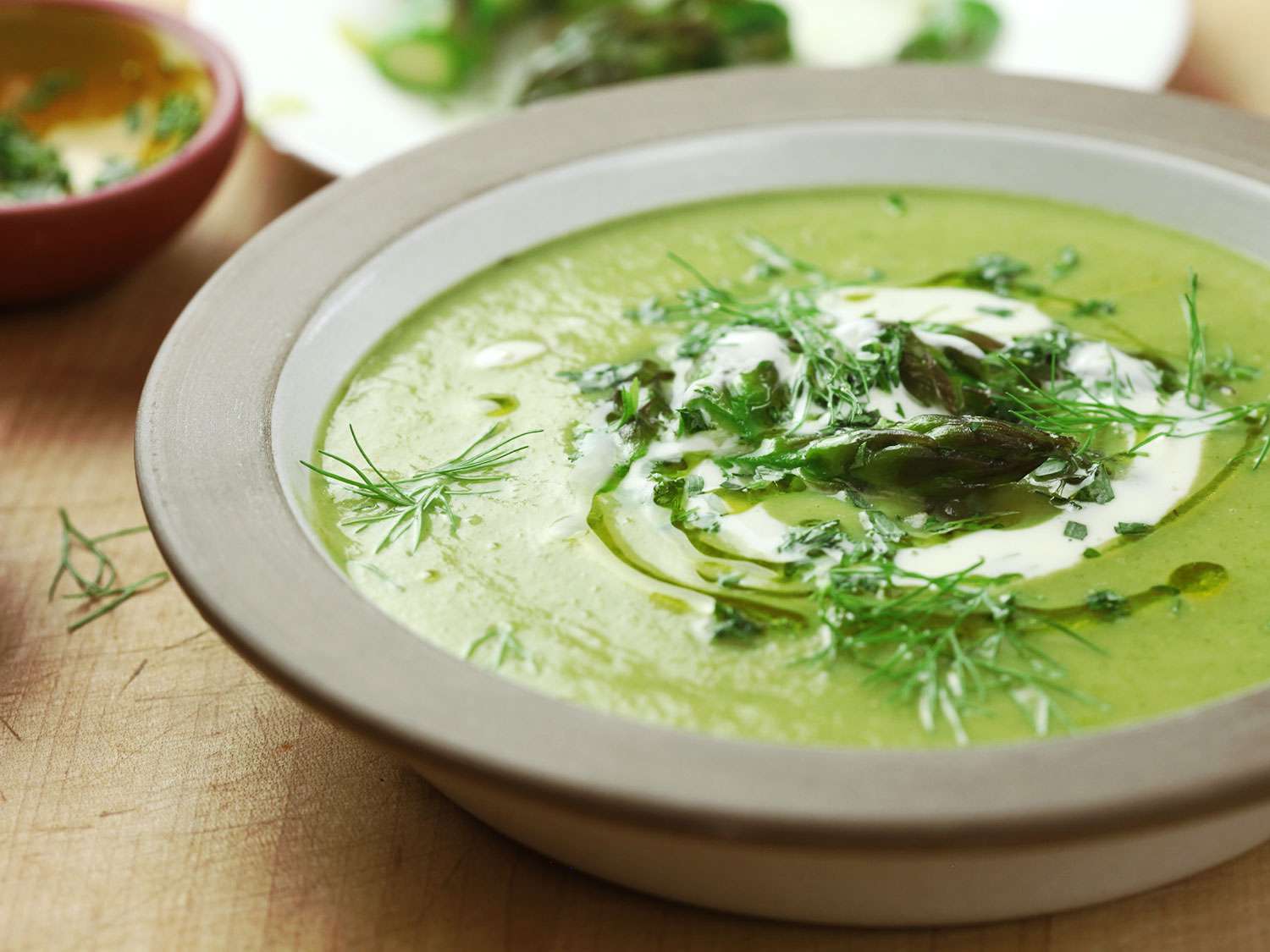 A bowl of cream asparagus and tarragon soup chopped tarragon,fennel frond, asparagus tips, a drizzle of olive oil, and a touch of crème fraîche.