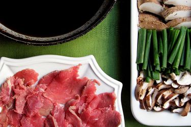 Overhead view of prepared meat and vegetables surrounding a pot for making sukiyaki.