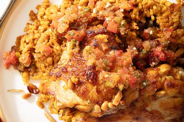 A closeup of a cooked dish with seasoned rice and chicken topped with a diced tomato mixture