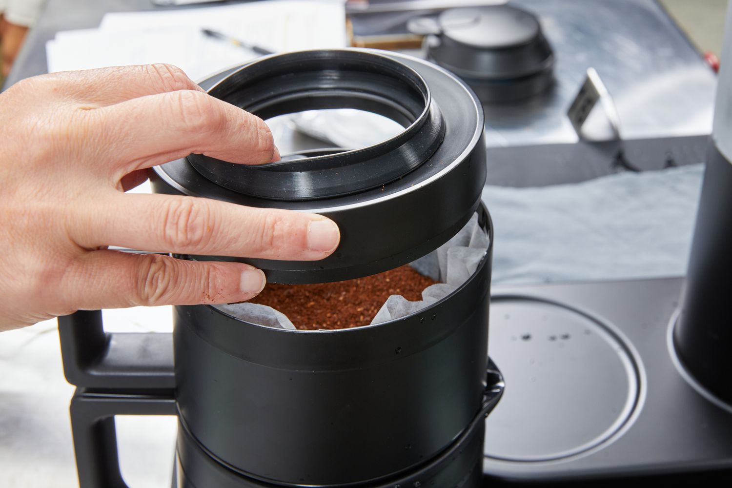 A hand puts the lid over the Ratio Six Coffee Maker's filter holder