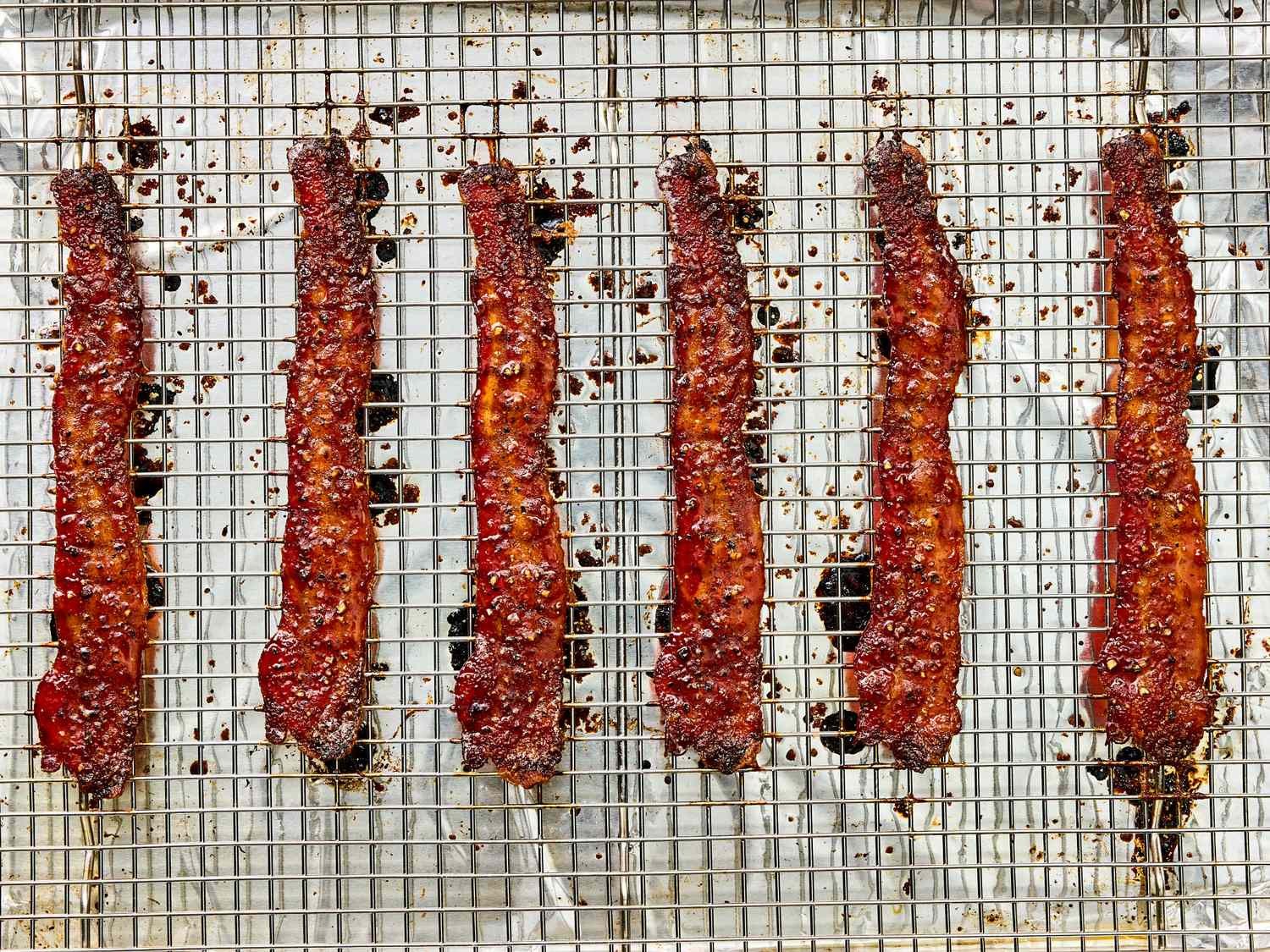 Six strips of seasoned bacon on a wire rack for cooking