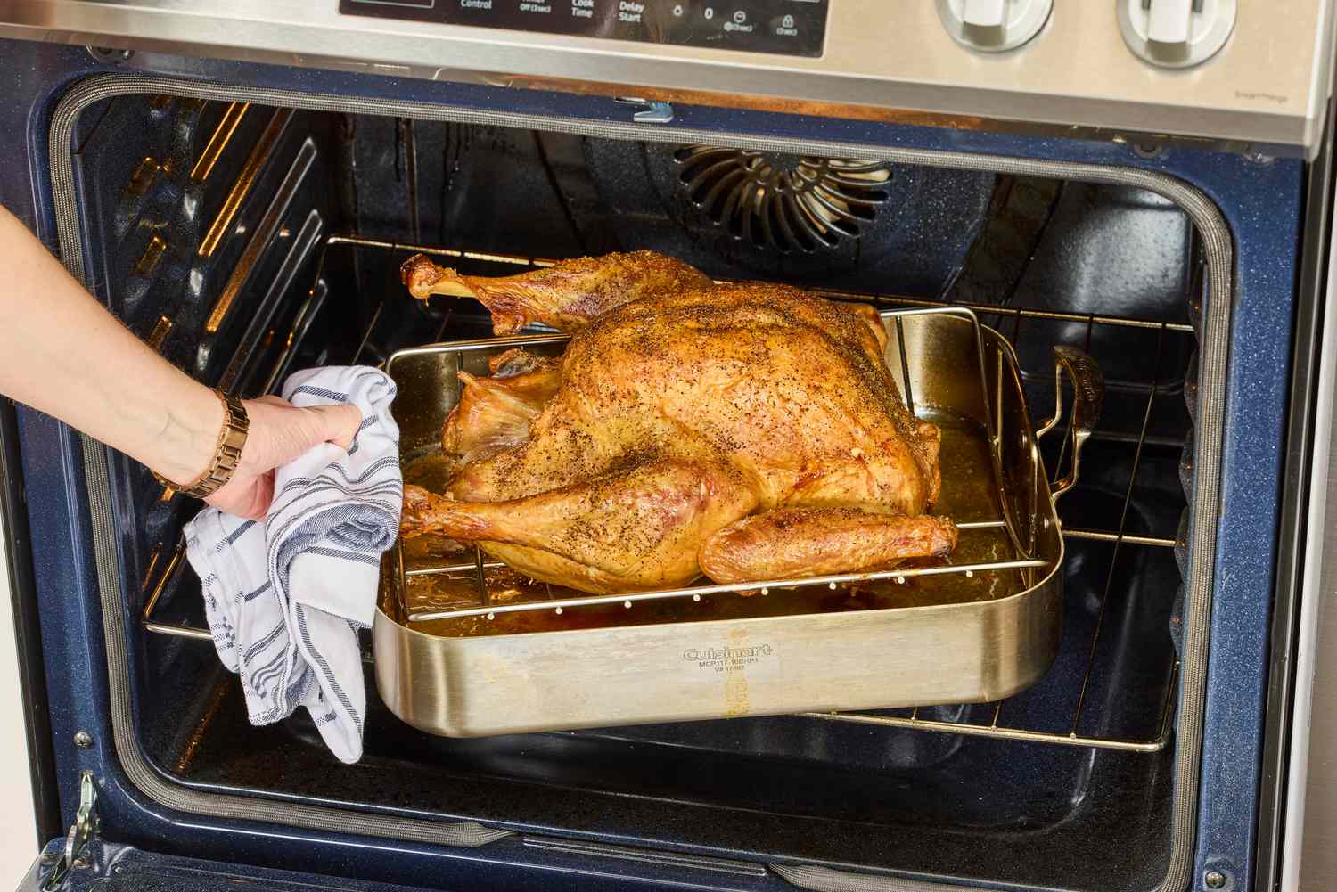 A person pulling a fully-cooked Williams Sonoma Willie Bird Turkey from an oven