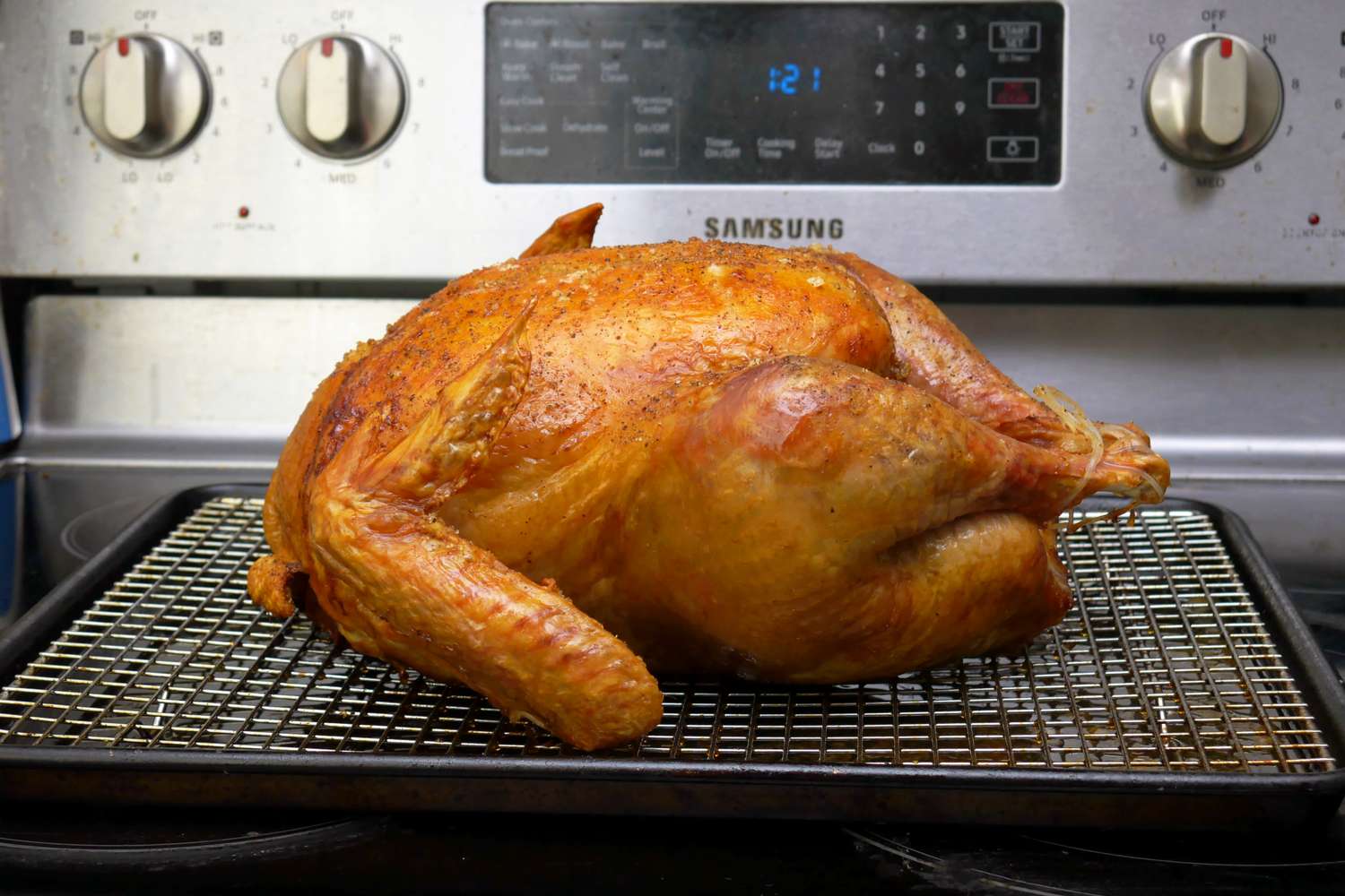 A roasted turkey placed on a cooling rack in front of an oven