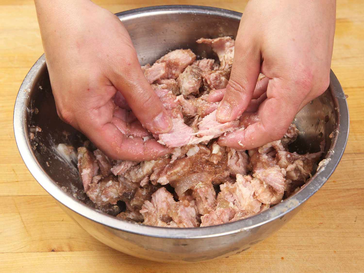 Shredding sous vide pork carnitas in a metal bowl before browning.