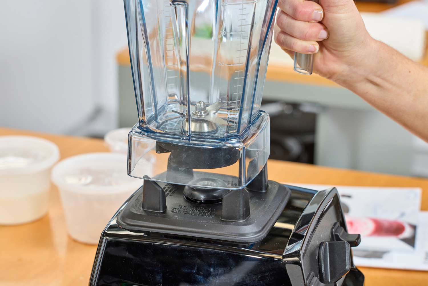 A hand lifting the Vitamix E310 Explorian Blender jar from the base