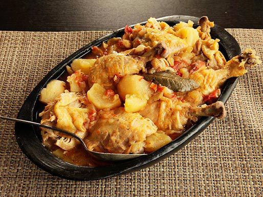 Black casserole dish filled with braised chicken and potatoes on brown placemat 