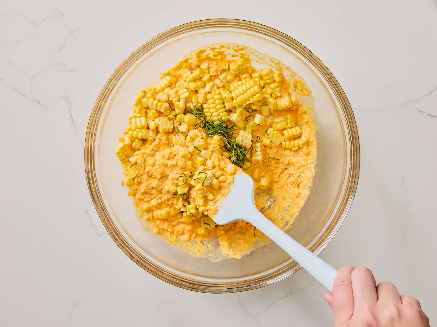 Mixing reserved corn kernels with blended mixture with spatula in glass bowl 