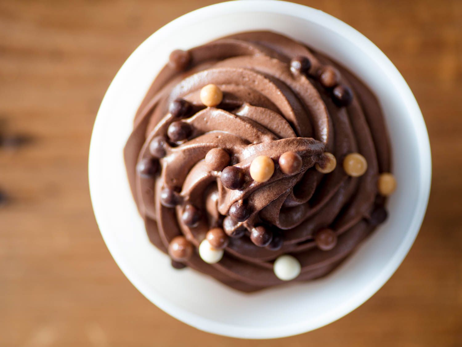 Overhead shot of a white dessert bowl filled with piped egg-free chocolate mousse, topped with chocolate pearls.