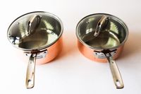 Two saucepans with lids featuring metal handles and clear glass tops
