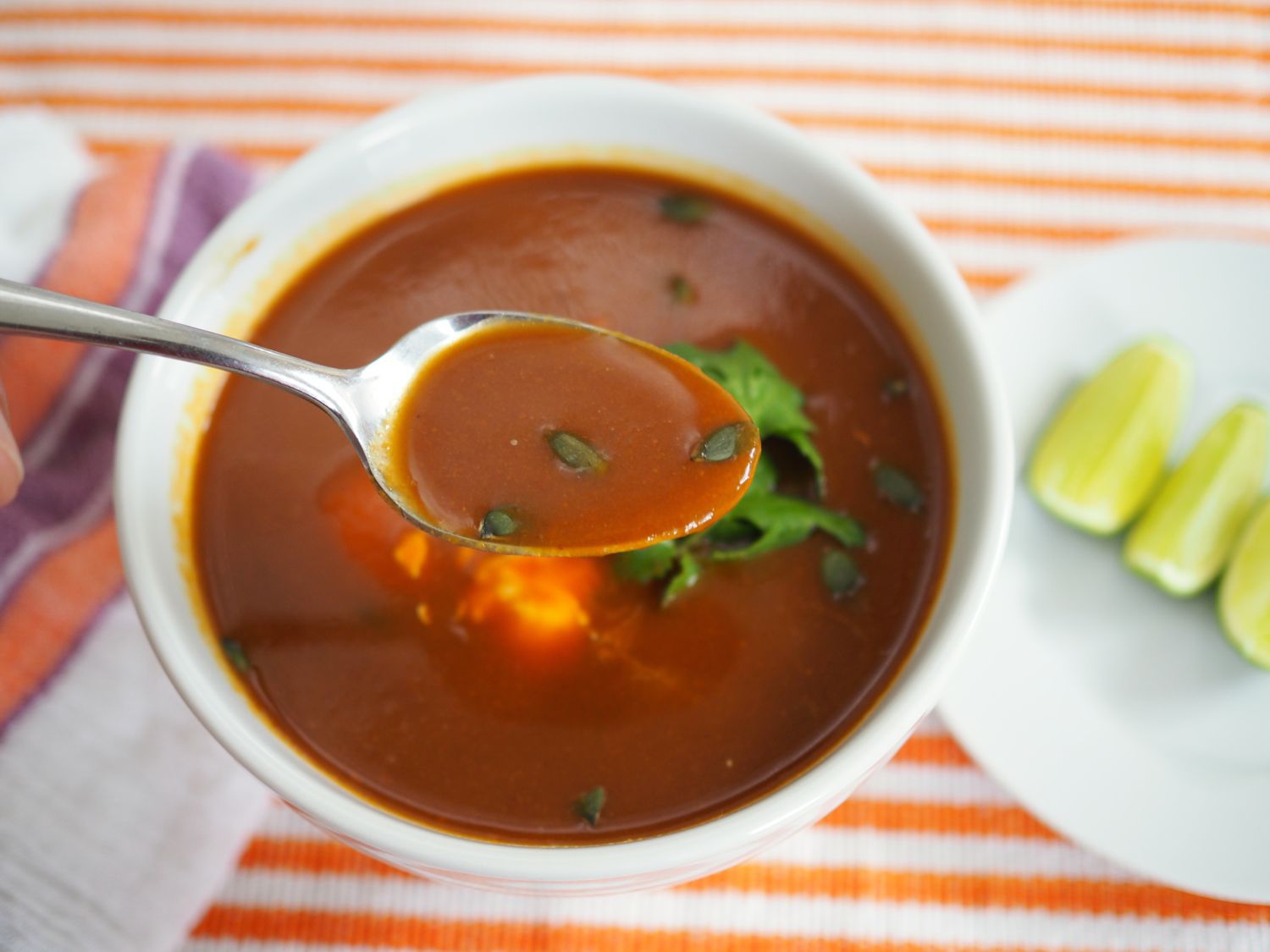 A spoon of butternut squash soup with ancho chile, crema, and pepitas lifted from the soup bowl.