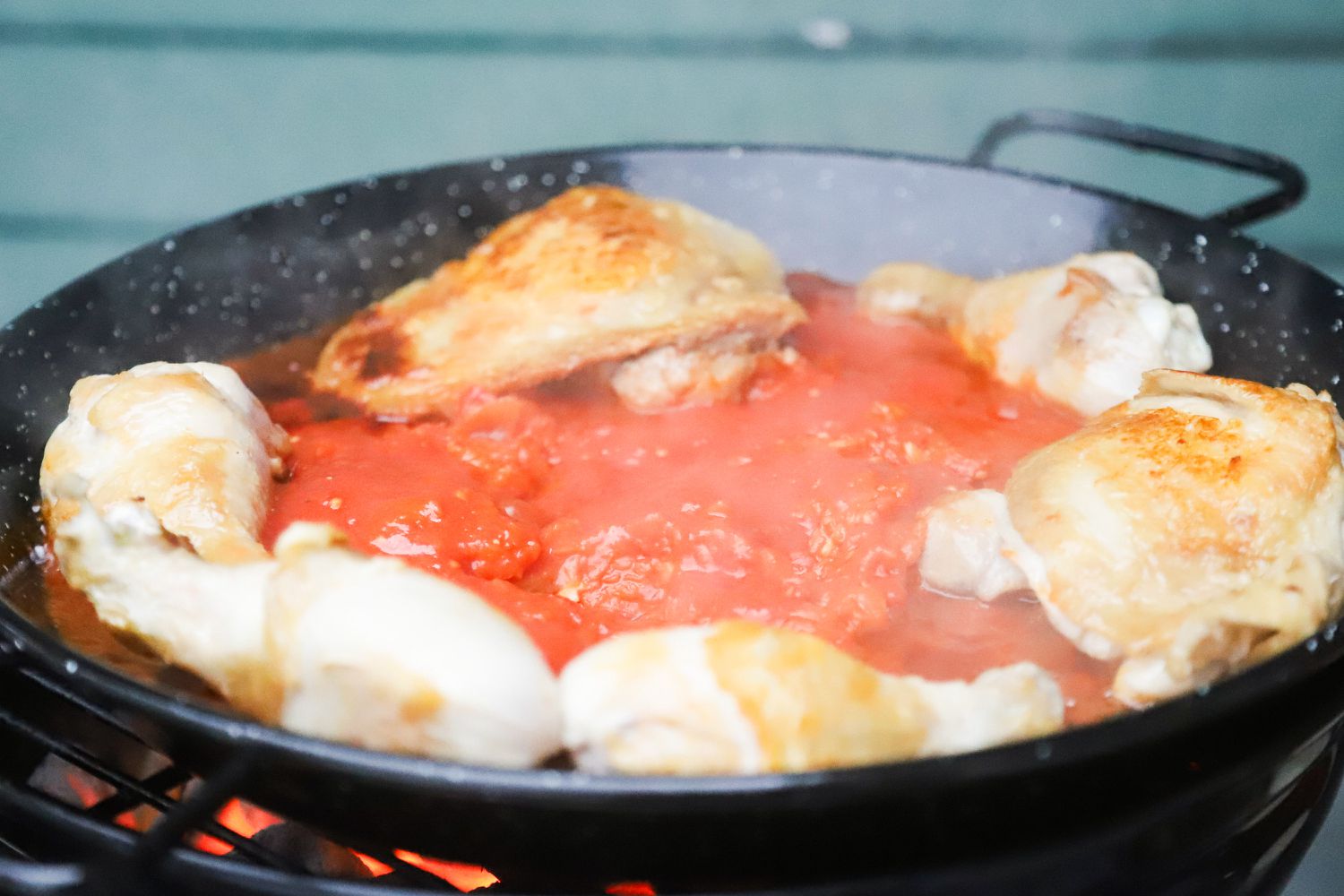 chicken and tomato cooking in a paella pan on a charcoal grill