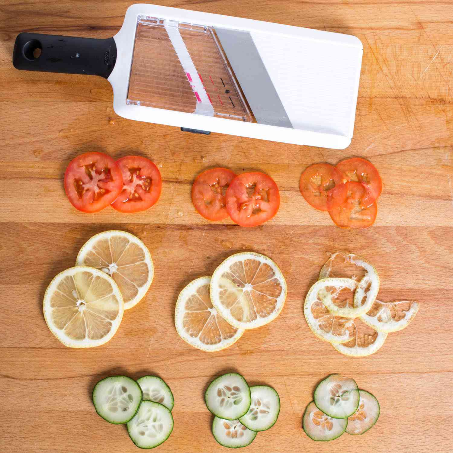 Slices of tomato, lemon, and cucumber next to the OXO handheld mandoline