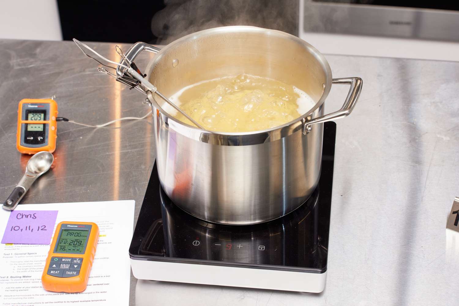 A pot of boiling water with a thermometer immersed, on an induction cooker, kitchen setup for cooking experiment