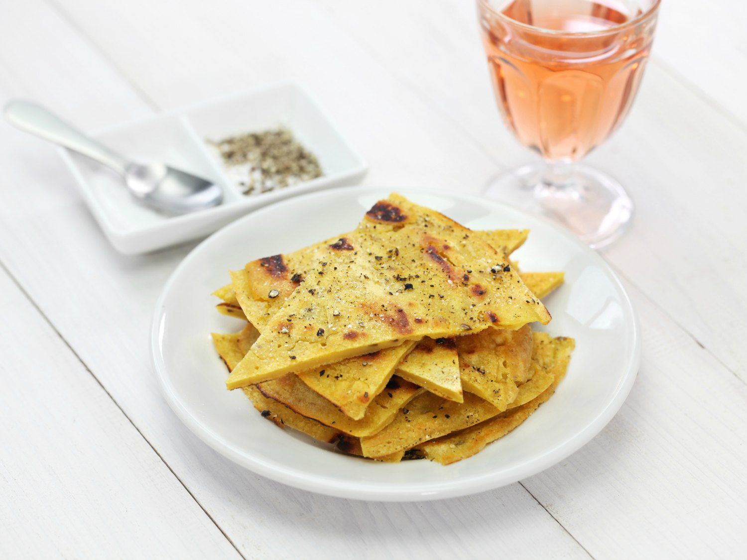 Wedges of socca, a farinata pancake, on a small white plate with a glass of rose wine next to it. 