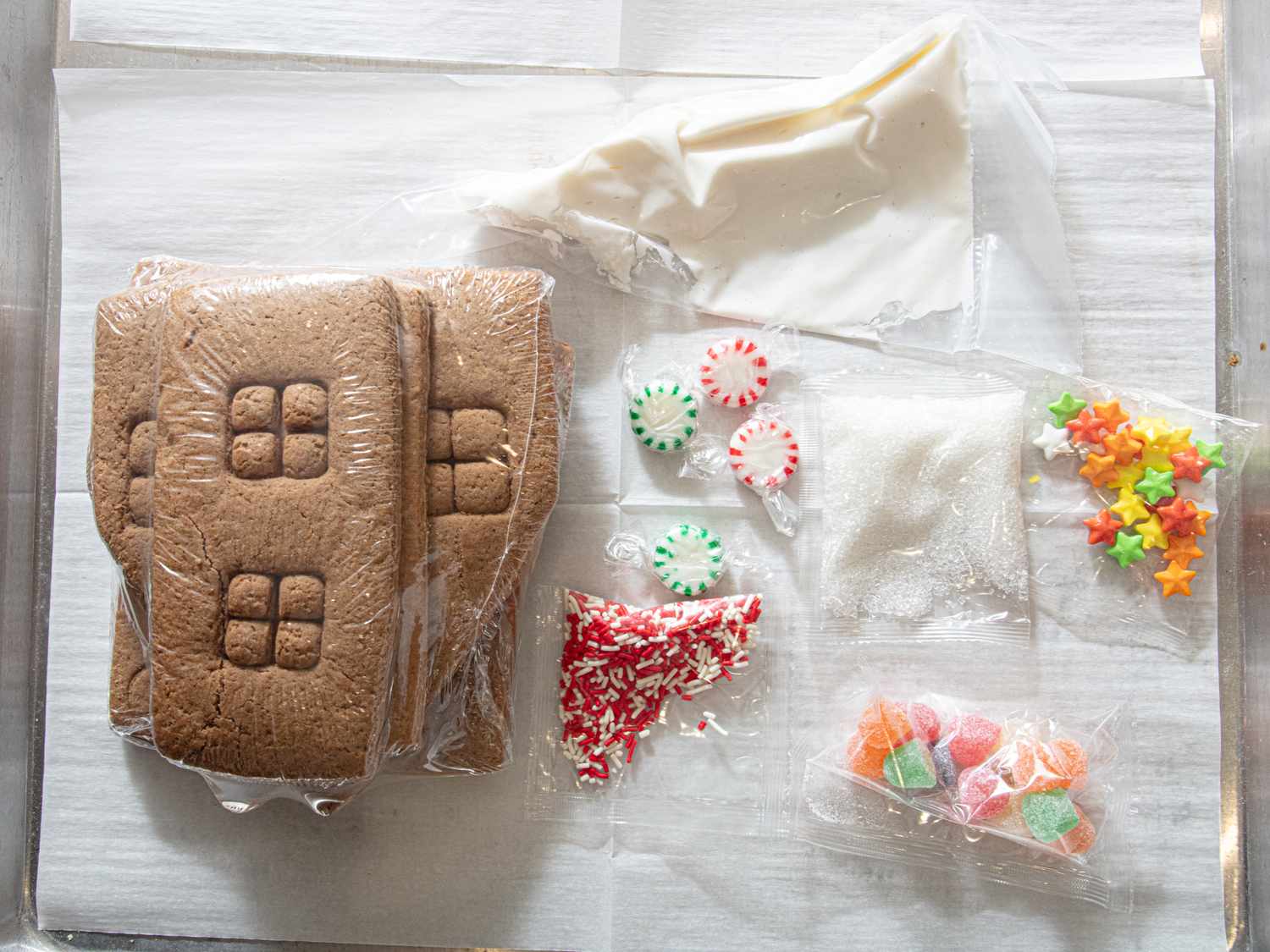 Gingerbread house components and decorations arranged on a surface includes icing candies and gingerbread panels