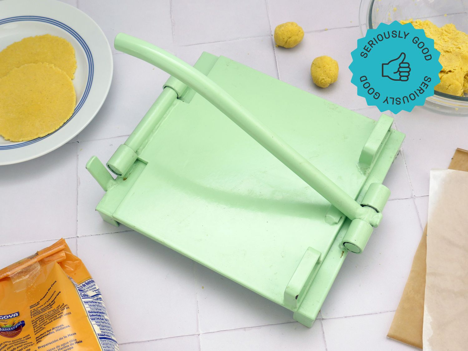 the masienda tortilla press with masa and tortillas on a white tile surface