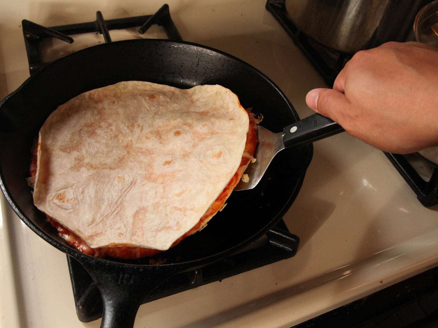 Flipping pizza quesadilla in a cast iron skillet with an offset spatula.