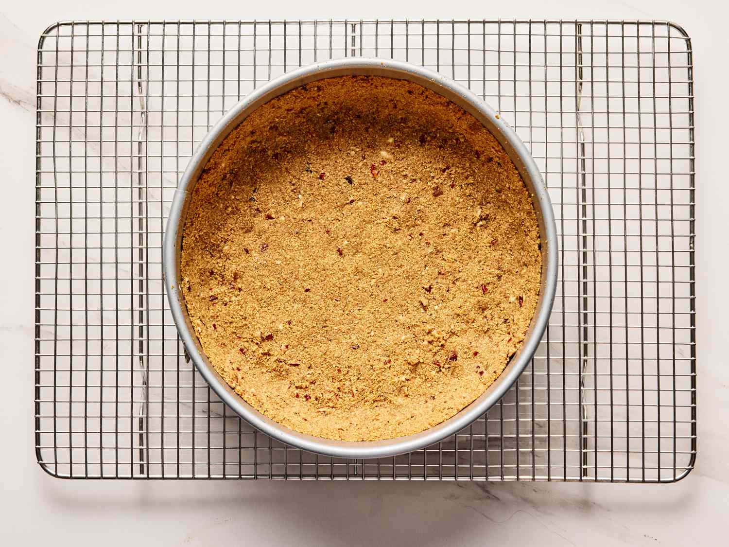 A springform pan filled with a crumb crust on a wire rack