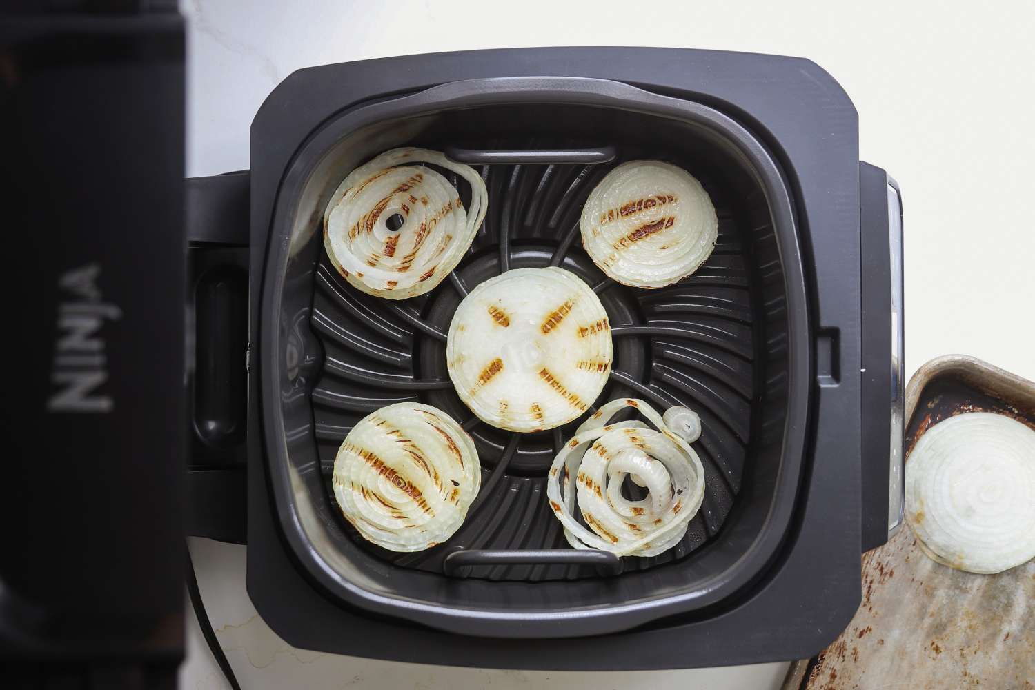 An indoor grill with grilled onion slices placed on its cooking surface
