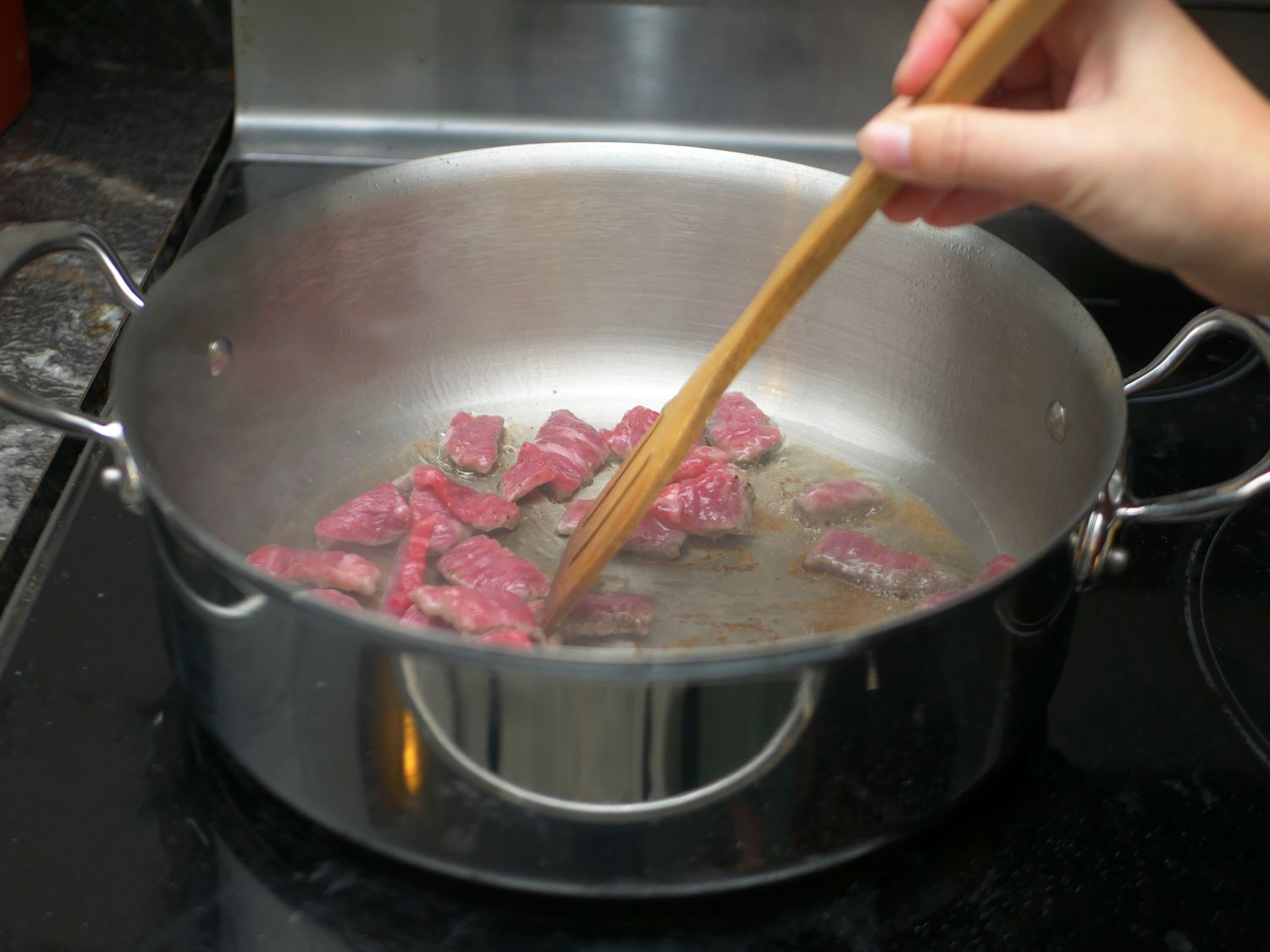 Using a wooden spoon to stir pieces of beef in a rondeau