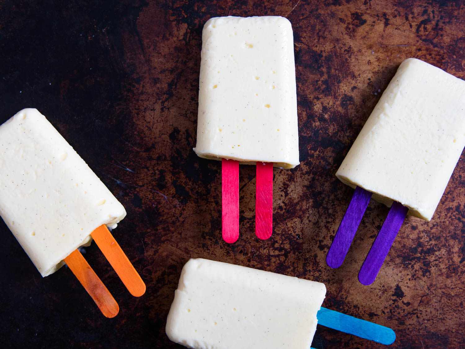 Overhead view of 4 vanilla pudding pops on a seasoned baking sheet.
