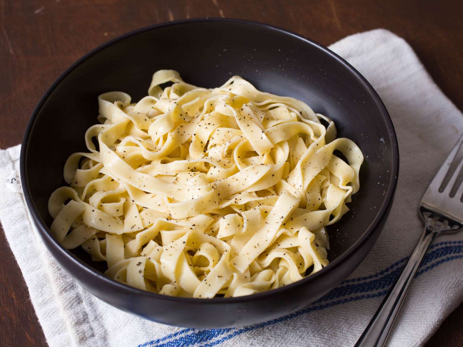 A bowl of fresh pasta ribbons in sauce sprinkled with black pepper.