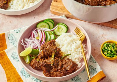 A plate with rice beef curry cucumber slices lime wedge and red onions served with a fork