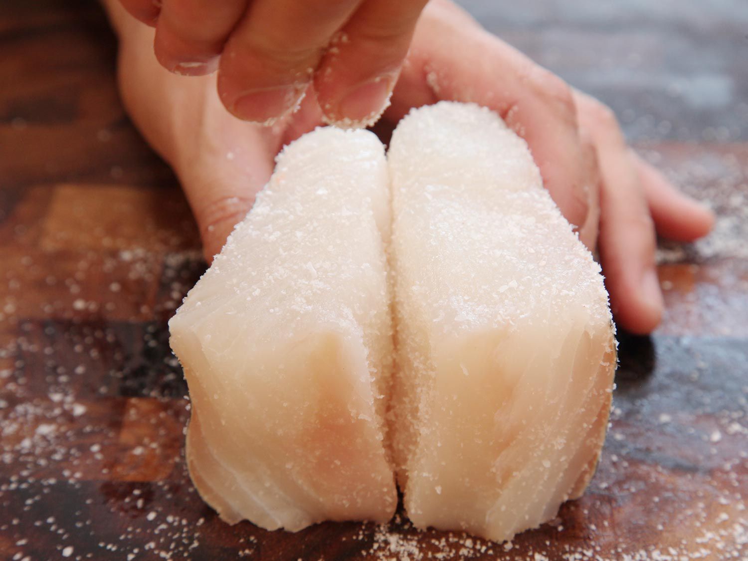 Seasoning raw halibut on all sides with salt to dry brine the fish before cooking. 
