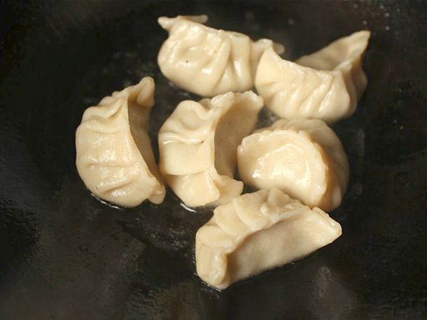 Six dumplings pan frying in a seasoned pan.